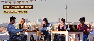Studierende sitzen auf einer Terrasse mit Blick über die Stadt und arbeiten gemeinsam an Laptops und Notizen unter bunten Wimpeln.