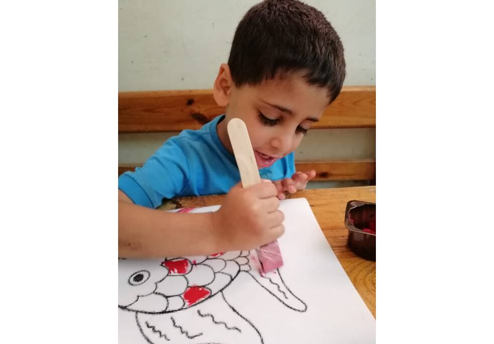 Ein Junge sitzt an einem Tisch und malt ein Bild aus. 