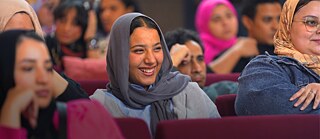 فتاة تجلس بين الحضور، تبتسم وتتابع الحديث باهتمام.