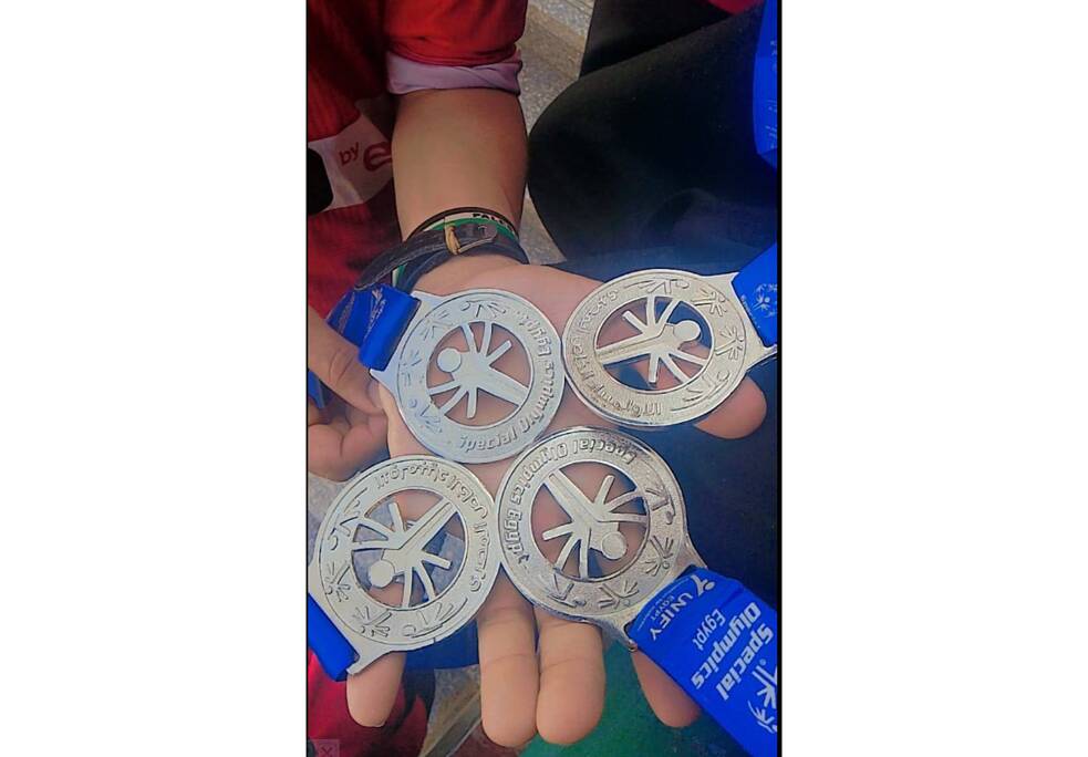 Zwei offene Kinderhandflächen auf denen 4 Medaillen mit blauen Bändern liegen. 