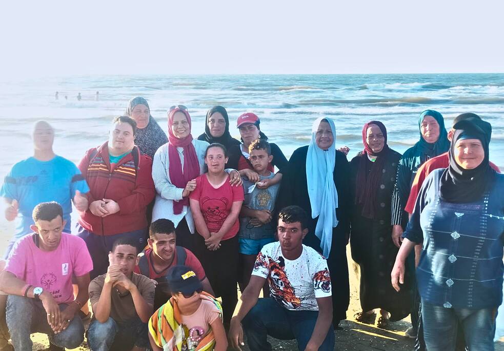 Eine Gruppe von Kindern und Erwachsenen am Strand. Sie posieren für ein Foto. Im Hintergrund sieht man das Meer.