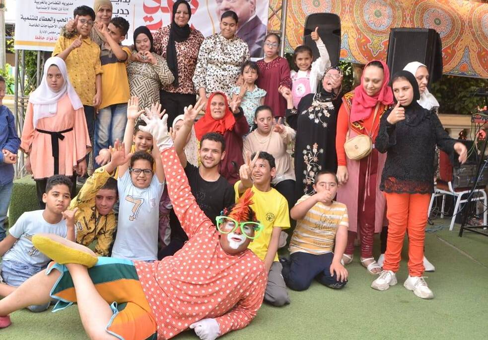 Eine Gruppe von Kinder posiert für die Kamera. In der Mitte am Boden liegt ein Mann, der sich als Clown verkleidet hat.