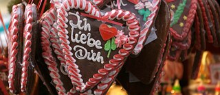   Lebkuchenherzen auf einem Marktstand, eines mit der Aufschrift ‚Ich liebe Dich‘ in weißer Zuckerschrift.