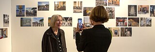 Im Vordergrund: die Künstlerin Christina Kubisch bei der Eröffnung der Ausstellung "Electrical Jubilee" am 23.05.2025 im Goethe-Institut Rom; im Hintergrund ausgestellte Fotos auf weißer Wand