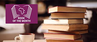 An open book in front of a book shelf. The book of the Month logo is right above that open book. 