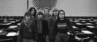 Un grupo de mujeres posa en una amplia sala oficial de sesiones, reconocible por su arquitectura característica y el emblemático águila federal en la pared, lo que indica un entorno político. Las personas se encuentran en el centro del espacio, rodeadas de asientos y mesas vacías que evocan un ambiente parlamentario.