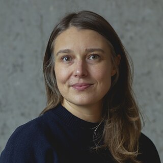 Elisabeth Kimmerle, aux cheveux bruns mi-longs, devant un fond gris uni. Elle regarde la caméra et porte un pull foncé