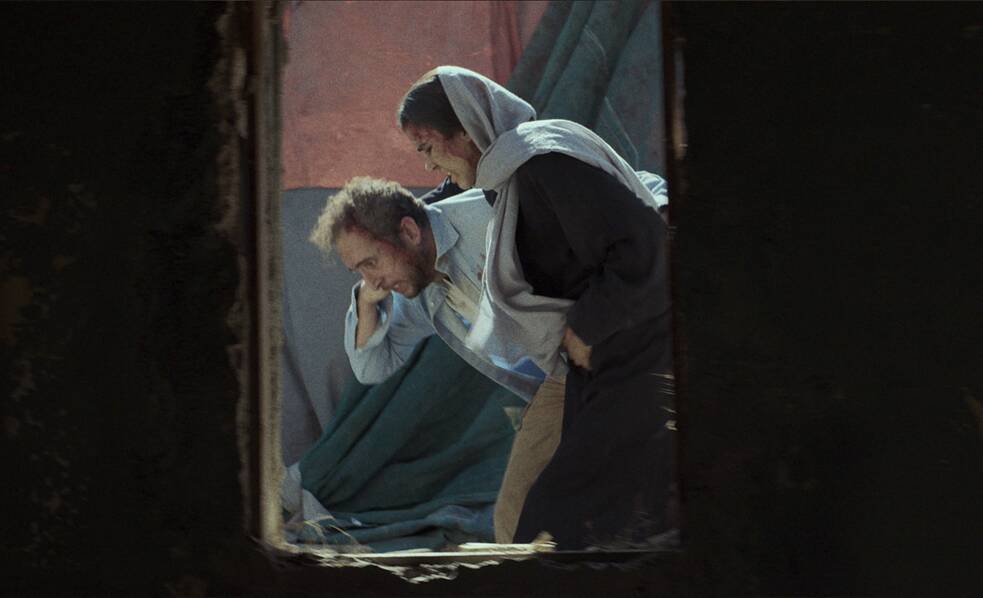 من خلال نافذة مفتوحة، يمكنك رؤية رجلين يسندان امرأة، وكلاهما ينزف من رأسه، وهما يمران.