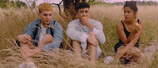 Drei Personen essen Pfirsiche, während sie auf einem Feld sitzen. 