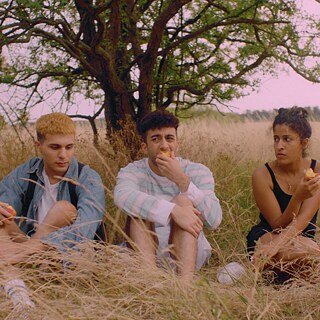 Drei Personen essen Pfirsiche, während sie auf einem Feld sitzen. 