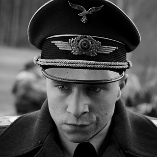 Foto eines Mannes in Nahaufnahme, auf den ein anderer mit einer Waffe zielt. 