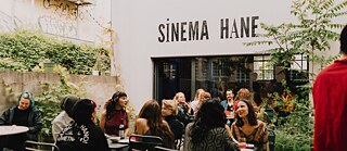 Gruppe junger Menschen sitzt im Hof des Sinema Hane und unterhält sich.
