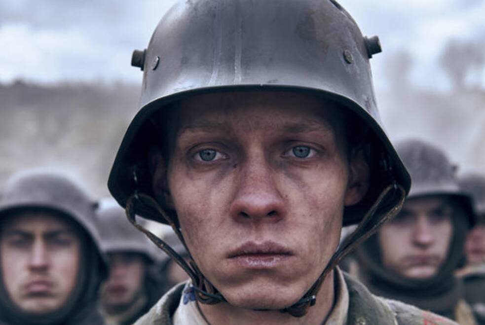 Standbild aus „Im Westen nichts Neues“: Ein junger deutscher Soldat des Ersten Weltkriegs mit Helm blickt ernst nach vorn. Sein Gesicht ist von Schmutz bedeckt. Hinter ihm stehen weitere Soldaten in ähnlichen Uniformen, unscharf im Hintergrund. Das Licht ist gedämpft, die Szene spielt im Freien. Der Film, die dritte und erste deutsche Verfilmung von Erich Maria Remarques Roman, ist mit neun Nominierungen und vier gewonnenen Oscars der bislang erfolgreichste deutsche Beitrag bei den Academy Awards.