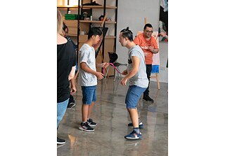 Deux adolescents se font face, chacun tenant un cordon rose. Derrière et devant eux, d'autres adolescents font de même.