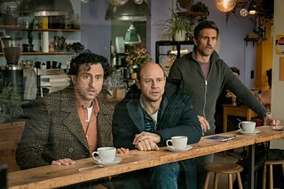 Still Frame from the Netflix Germany Series "Dudes": Moritz Führmann; Serkan Kaya; Tom Beck staring in diesbelief through a window from inside a coffee shop.
