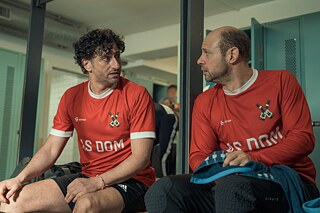 Still Frame from the Netflix Germany Series "Dudes": Alphamännchen; Moritz Führmann; Serkan Kaya in soccer jerseys sitting on a stadium bench.