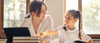  A woman and a child are seated at a table, focused on a books in front of them.