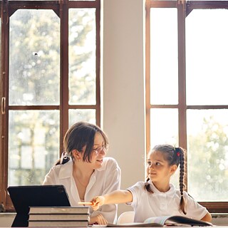  A woman and a child are seated at a table, focused on a books in front of them.