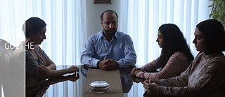 Ein Mann sitzt vor Kopf eines Esszimmertisches. Links neben ihm sitzt eine Frau, rechts neben ihm zwei jüngere Frauen. Er schaut nach rechts, die Frauen blicken nach unten. Am linken Rand des Bildes steht "CINE CLUB GOETHE".