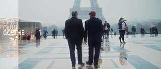 Zwei Männer laufen auf einem nebeligen Platz in Richtung des Eiffelturms.