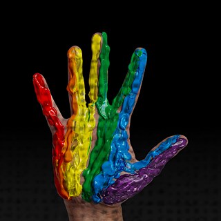 Hand raised against a black background, coated in thick rainbow-colored paint from red to purple.