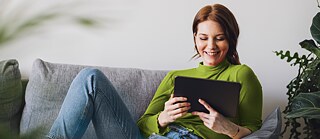 Nainen lukee e-kirjaa sohvalla.