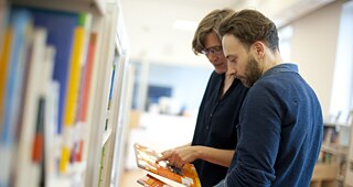 Zwei Personen schauen sich gemeinsam Bücher in einer modernen Bibliothek an.