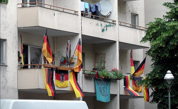 Deutschlandfahnen hängen an einer Hauswand an Balkonen. 