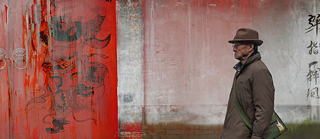 A still from Zhou Fei’s video work Jinhua Road (Road of Golden Splendor) shows a weathered red wall with traditional figure drawings and traces of time, history, and change.