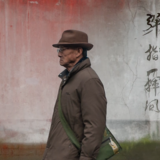 A still from Zhou Fei’s video work Jinhua Road (Road of Golden Splendor) shows a weathered red wall with traditional figure drawings and traces of time, history, and change.