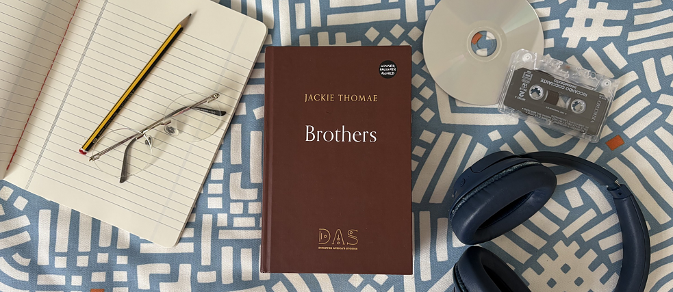 The book  'Brüder' lies on a chequered blanket alongside a notebook, a pencil, a pair of glasses, a CD, a cassette and a pair of headphones