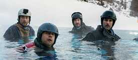 Standbild aus der Netflix Deutschland Original Serie „Alphamännchen“: Die vier „Alphamännchen“ – David Rott, Moritz Führmann, Serkan Kaya und Tom Beck – stehen in voller Skiausrüstung bis zur Brust in einem See in einer winterlicher Landschaft.