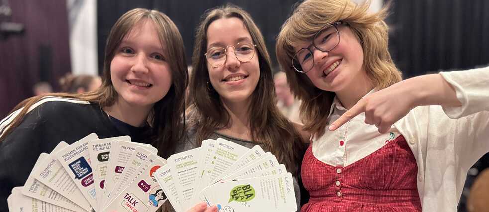 3 Schülerinnen präsentieren den Talk ohne Grenzen-Fächer.