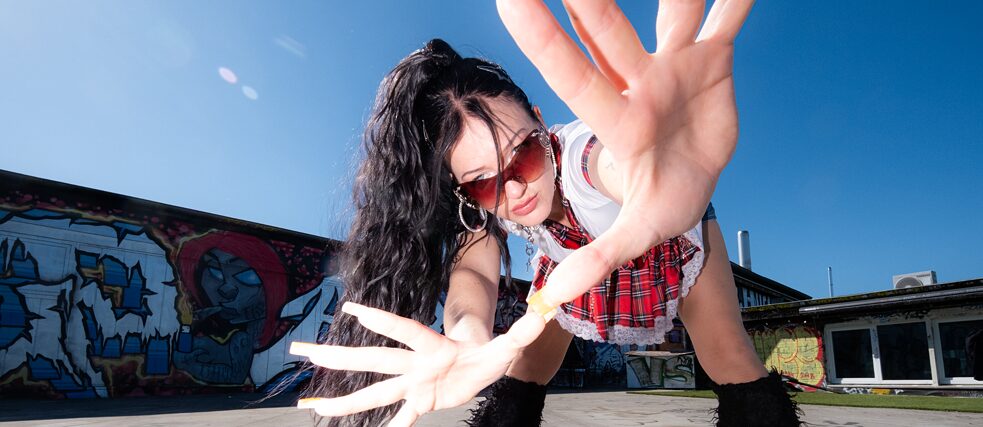 Artist Mariybu, black hair in a ponytail and sunglasses,  bending down and holding a hand with long fingernails close to the camera