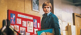 Alex Kerner (Daniel Brühl) steht vor einer „40 Jahre DDR“-Tafel und hält ein Foto in einem Innenraum mit DDR-Elementen.