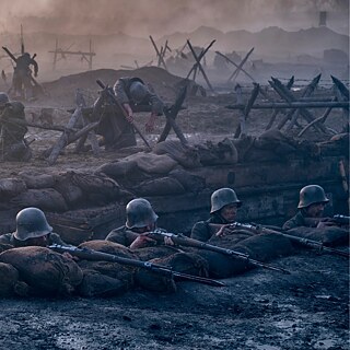 Das Bild zeigt mehrere Soldaten in einem Schützengraben, die mit ihren Gewehren auf den Feind zielen. Vor ihnen liegen Sandsäcke als Schutz. Im Hintergrund sind zerstörte Barrikaden aus Stacheldraht, Schlamm und Trümmern zu sehen.