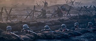 Das Bild zeigt mehrere Soldaten in einem Schützengraben, die mit ihren Gewehren auf den Feind zielen. Vor ihnen liegen Sandsäcke als Schutz. Im Hintergrund sind zerstörte Barrikaden aus Stacheldraht, Schlamm und Trümmern zu sehen.