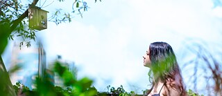 Links im Bild hängt ein Vogelhaus in einem Baum, rechts davon ist eine Person zu sehen, die nachdenklich auf das Vogelhaus schaut