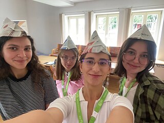 Teilnehmende des Seminars präsentieren ihre kreativen Gruppenarbeiten mit selbst gebastelten Papierhüten.