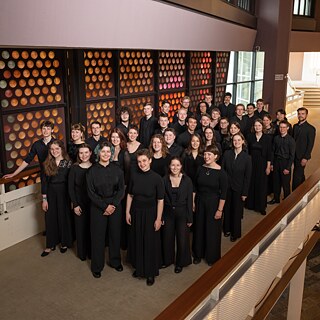 Members of the Bundesjugendchor stand on staircases and walkways in a modern building, dressed in black concert attire for a group portrait during the choir’s South Africa tour.