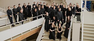 Members of the Bundesjugendchor stand on staircases and walkways in a modern building, dressed in black concert attire for a group portrait during the choir’s South Africa tour.