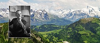 Ein Bild von Autor Thomas Mann der interessiert dreinschaut und sich die Hand an das Kinn hält. Dahinter ist eine schweizer Alpenlandschaft.
