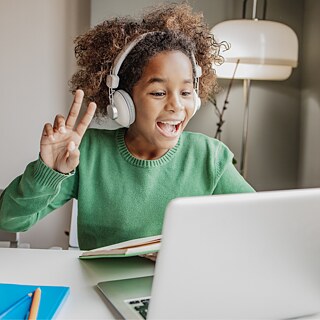Young student wearing headphones and waving during an online German course for kids with the Goethe-Institut USA