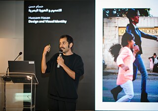 Eine Person hält einen Vortrag auf einer Bühne und präsentiert Inhalte zu Design und visueller Identität vor einer großen Projektionsfläche.