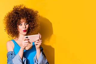 Giovane donna sorridente con smartphone su sfondo giallo