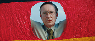 A man looks through a hole cut out of a German flag.