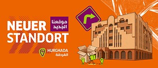 Ankündigungsbanner auf orangefarbenem Hintergrund für einen neuen Standort in Hurghada mit der Aufschrift „NEUER STANDORT / موقعنا الجديد“ sowie Grafiken eines Gebäudes, eines Kartons und eines Richtungszeigers.