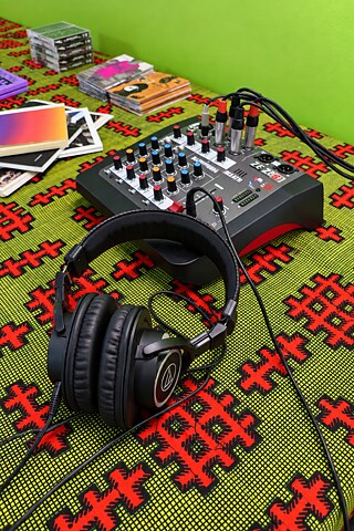 Sonic-Library-Setup mit Kopfhörern, Mischpult, Publikationen und Kassetten auf einem gemusterten Tisch.