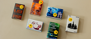 Sechs Bücher der Shortlist des Deutschen Buchpreises 2026 liegen auf einer hellen Oberfläche und sind aus der Vogelperspektive fotografiert.