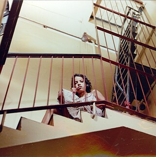 Persona sentada en un descanso de escalera interior detrás de una baranda metálica.